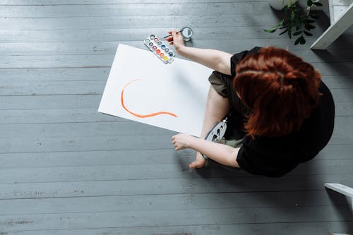A Person Sitting on a Wooden Floor and Painting on a Paper