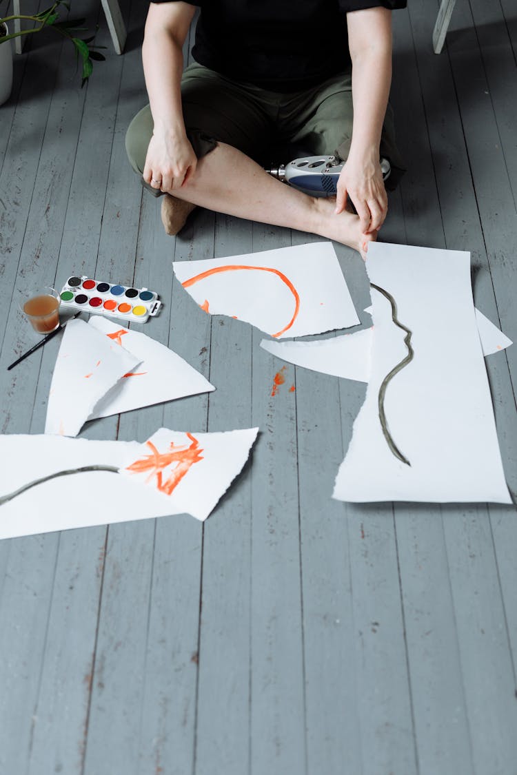 An Artist Sitting Beside A Ripped Painting On The Floor