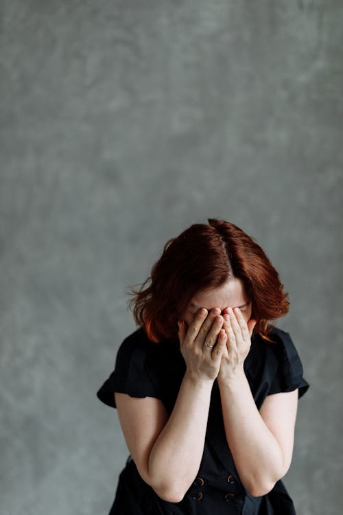 Free A woman feeling distressed and emotional, covering her face, against a textured concrete background, conveying themes of stress and sadness. Stock Photo