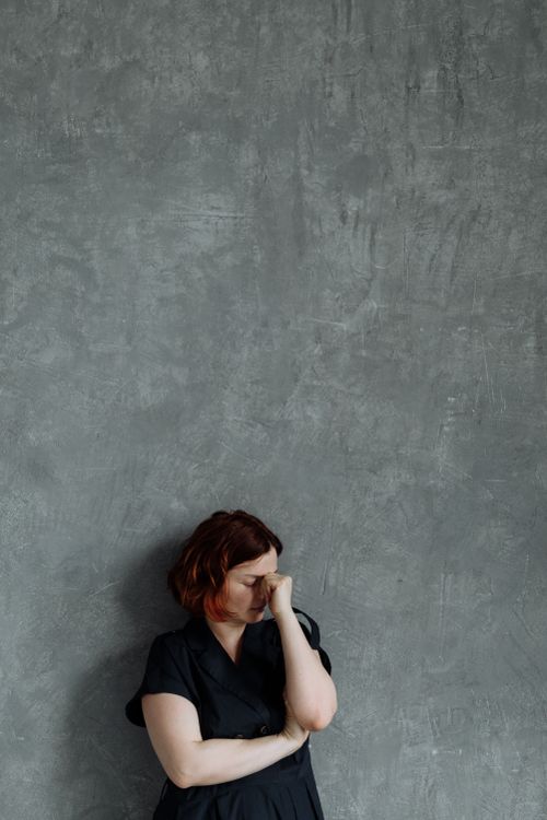 Free Pensive woman in black dress leans against textured gray wall, deep in thought. Stock Photo