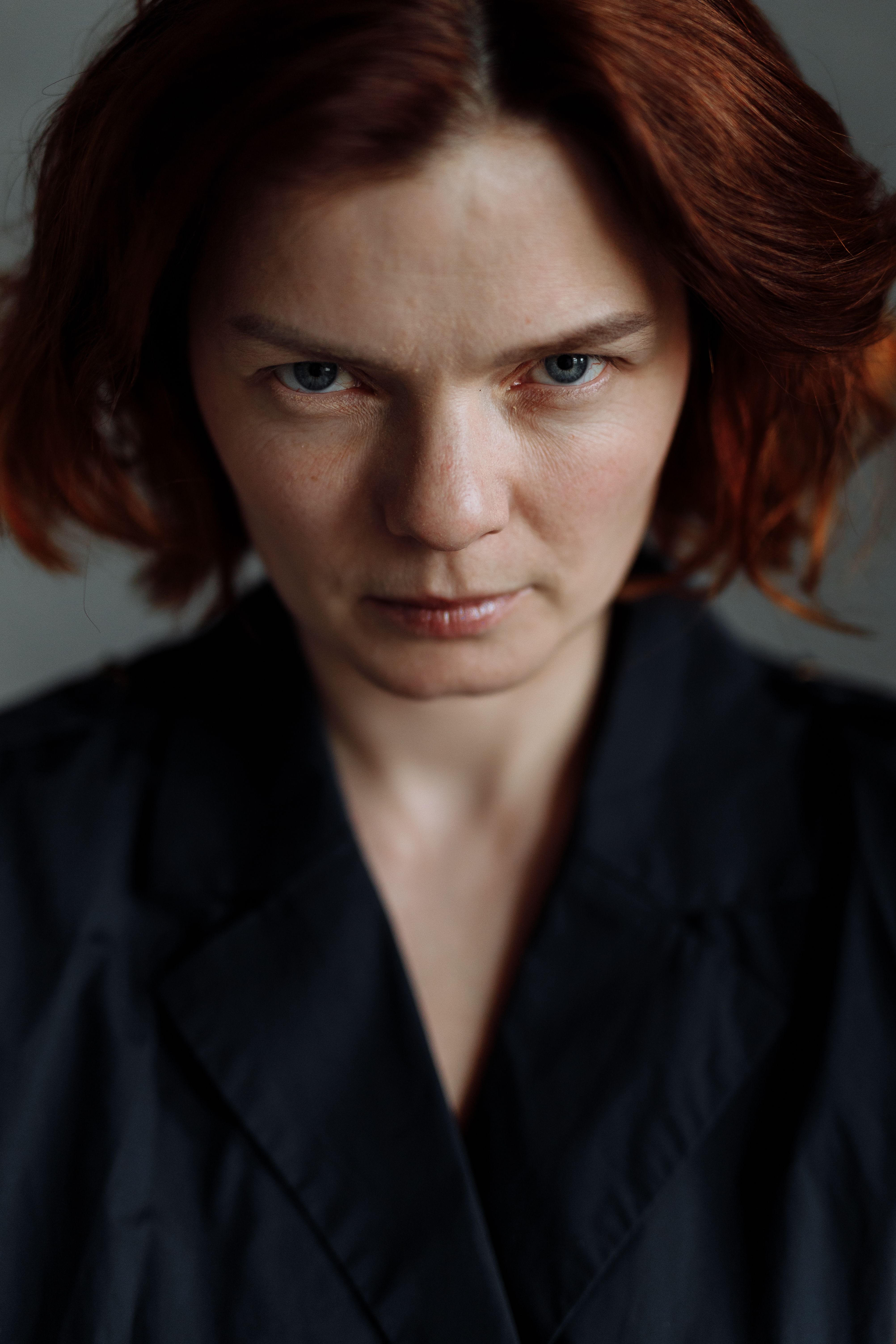 Close-up portrait of a woman with red hair wearing a black jacket, expressing intensity.