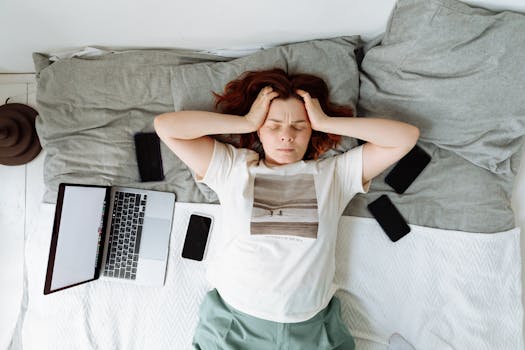 A distressed woman lying in bed surrounded by digital devices, showing signs of stress.