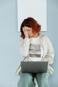 A young woman feeling stressed while sitting with a laptop indoors, depicting burnout.