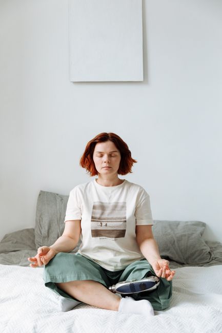 A woman sits cross-legged on a bed, meditating with eyes closed and a prosthetic leg visible.