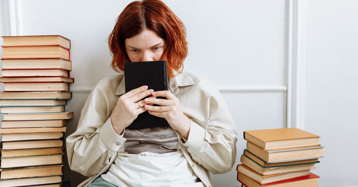 person holding smartphone with thoughtful expression, surrounded by scattered books and analog tools