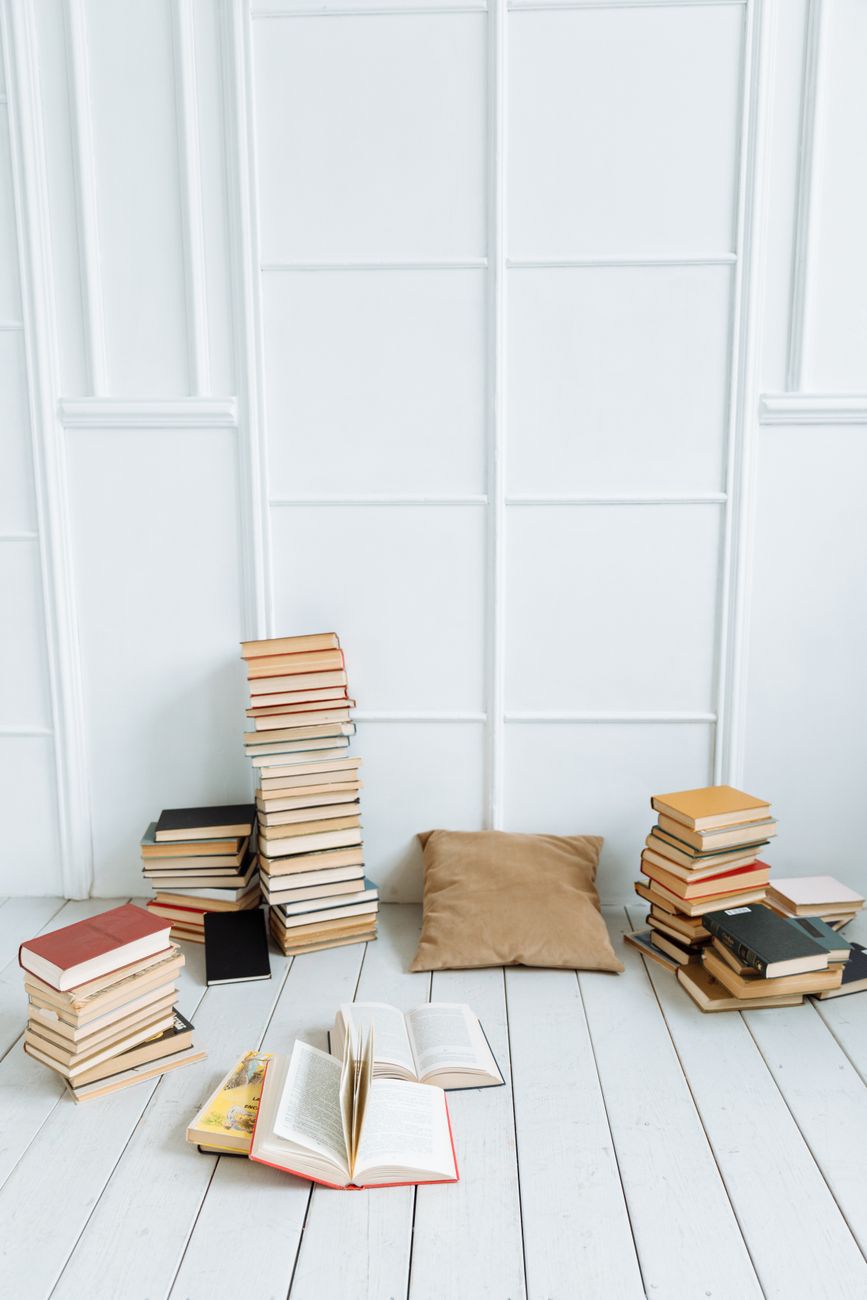 Vertical shot of stacked books and a pillow on a white wooden floor, ideal for educational or reading-themed content.