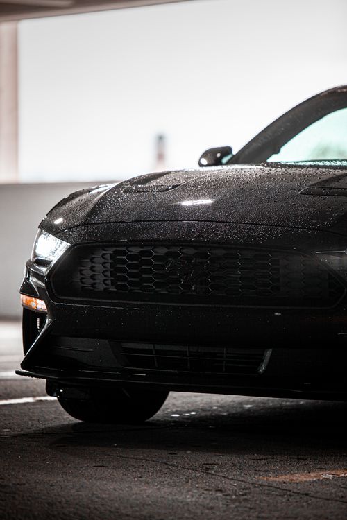 Free Close-up of a black car with raindrops on the hood, reflecting night lights. Stock Photo