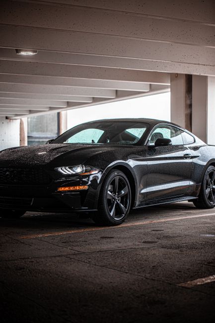 A stylish black Mustang sits parked in a dimly lit urban parking garage, showcasing its sleek design.