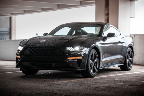 Free A shiny black car with raindrops parked in a covered urban parking area. Stock Photo