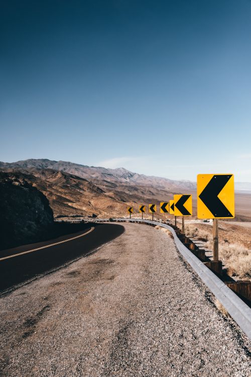 Free An empty winding road with curve signs through a dry, arid desert landscape. Stock Photo
