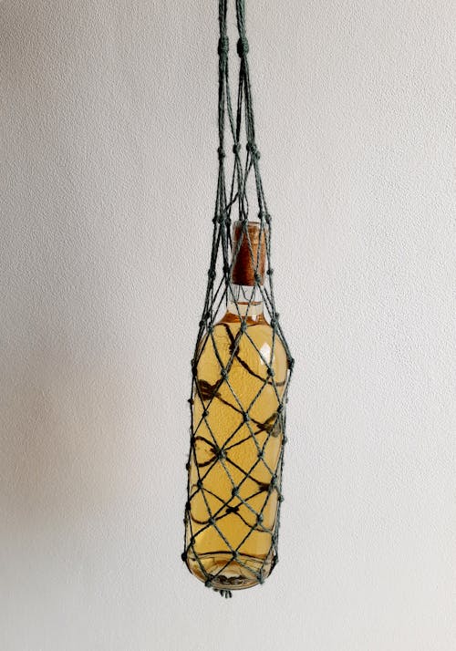 Hanging Bottle on a Net Bag with Yellow Liquid Near White Wall