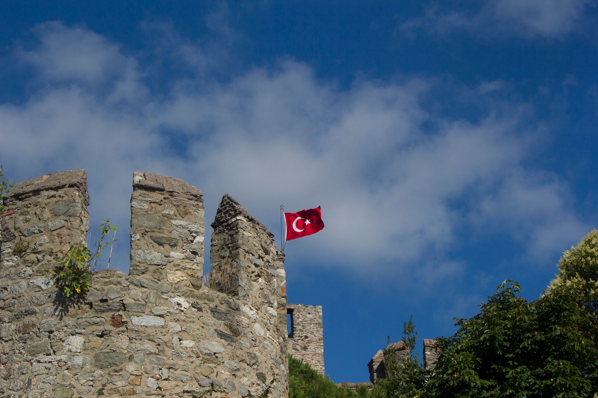 Stone fortress wall in Anadolu Kavağı, İstanbul with a Turkish flag waving under a blue sky.