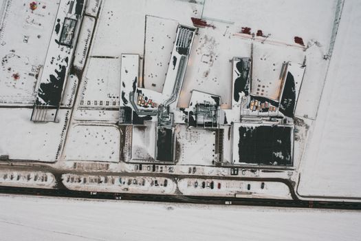 A top-down aerial view of a snow-covered industrial area in Poznań, Poland during winter.