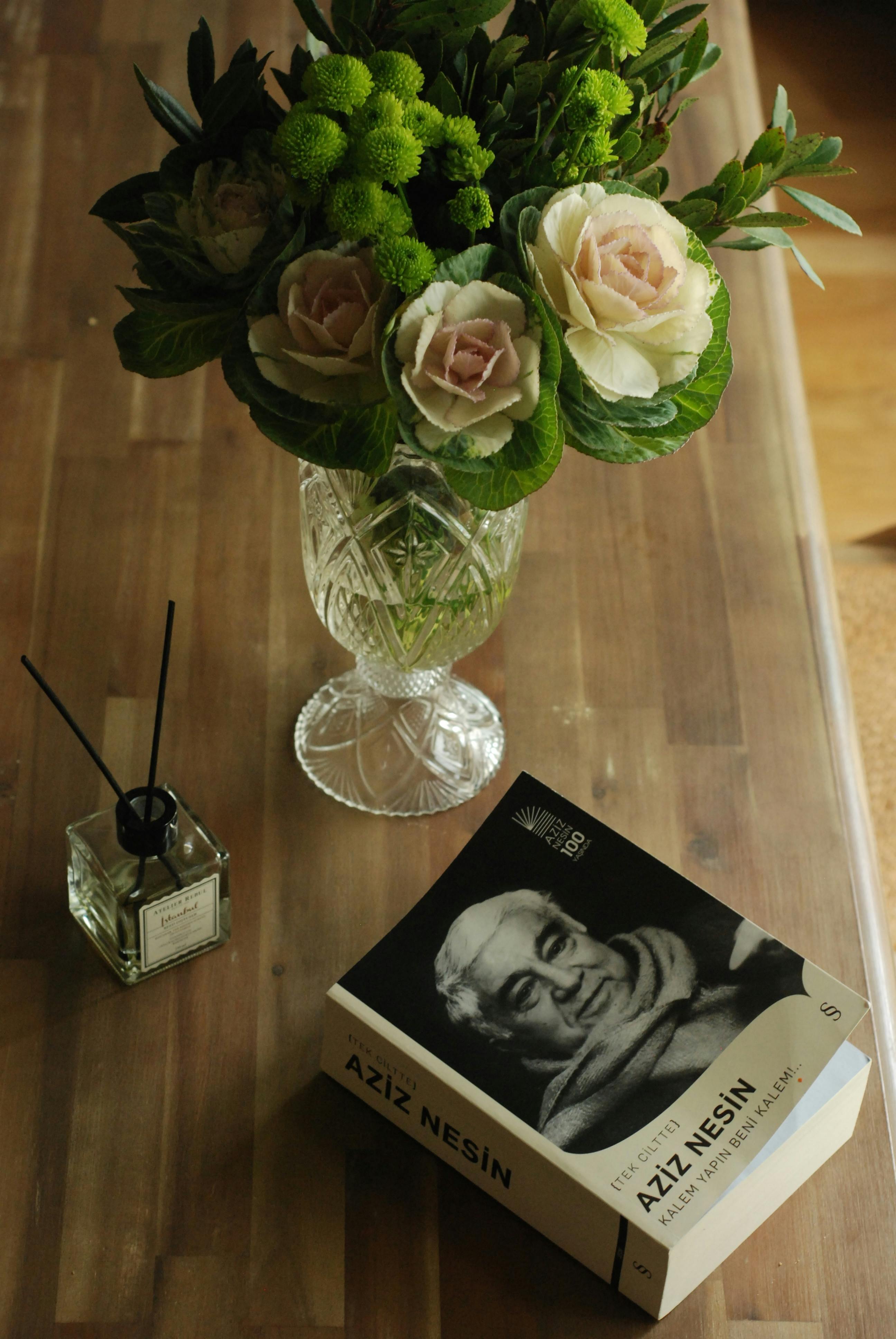 A sophisticated still life featuring a bouquet, book, and incense on a wooden desk.