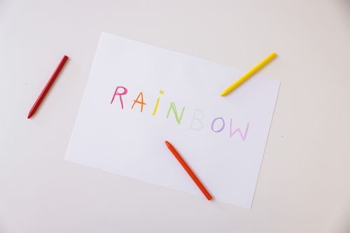 Free Top view of rainbow-colored crayon drawing on white paper with colored crayons on a white surface. Stock Photo