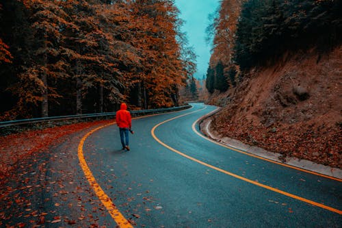 Unrecognizable man walking on road among autumn forest