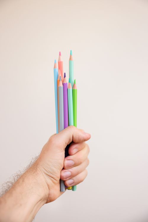 Free A hand holding vibrant colored pencils against a neutral backdrop, highlighting creativity and art. Stock Photo