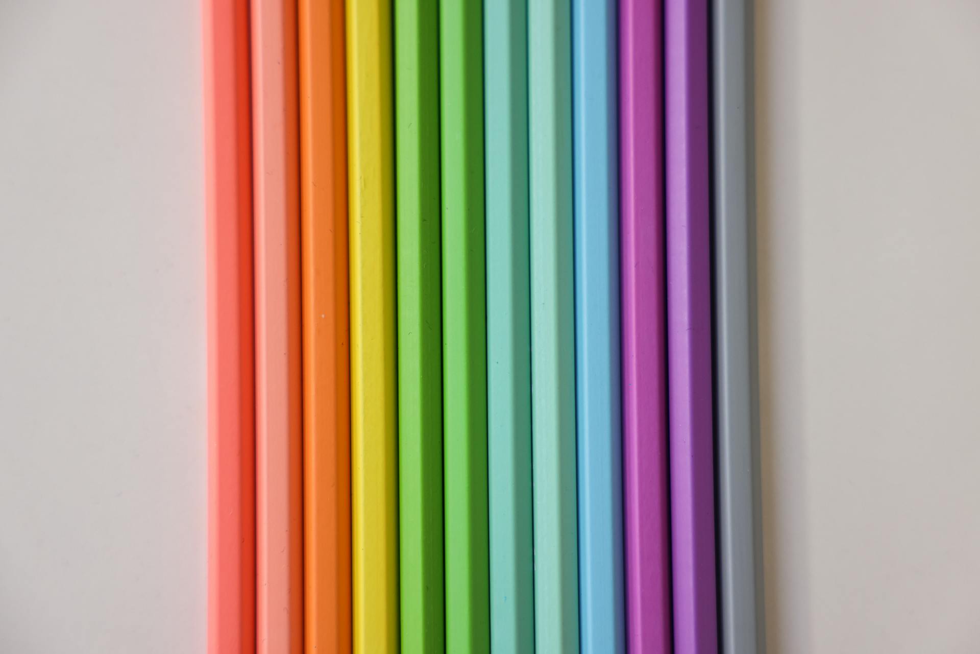 A neat arrangement of colorful pencils in rainbow order on a white surface.