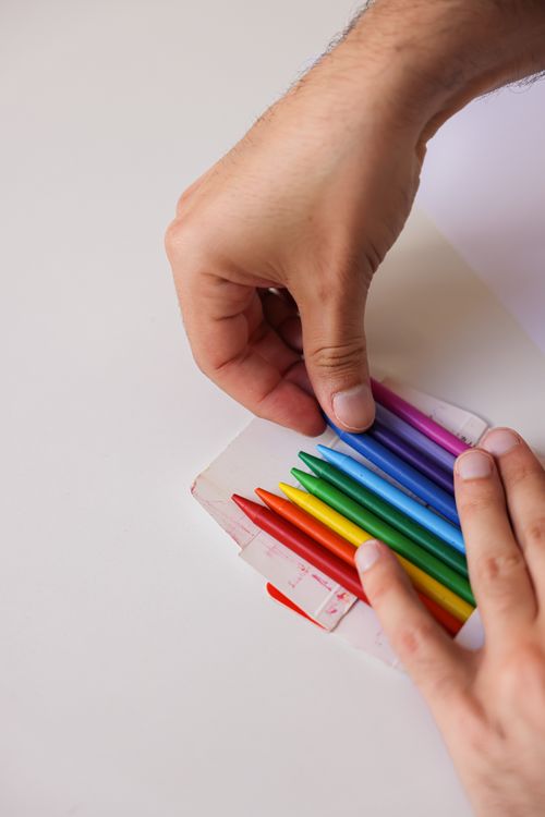 Free Hands arranging colorful colored pencils on a white surface in close-up view. Stock Photo