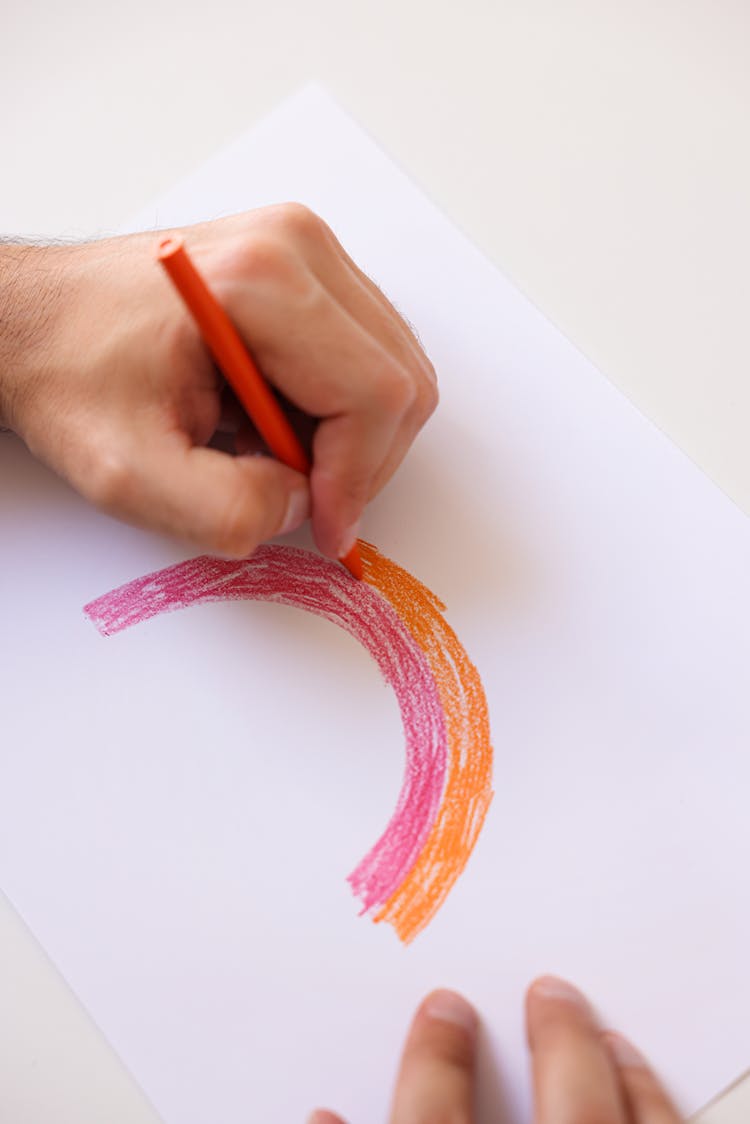 A Person Trying To Draw A Rainbow On A Bond Paper