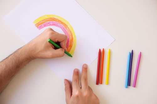 Free Hand drawing a colorful rainbow using crayons on white paper, showcasing creativity and art. Stock Photo