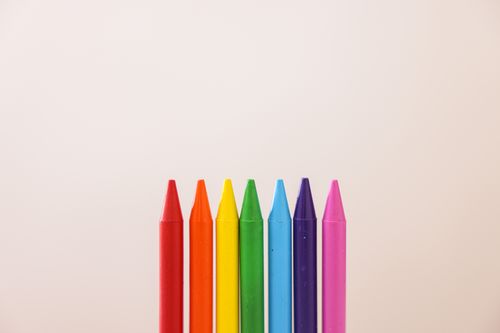 Free Brightly colored crayons arranged in a row on a neutral beige background. Stock Photo