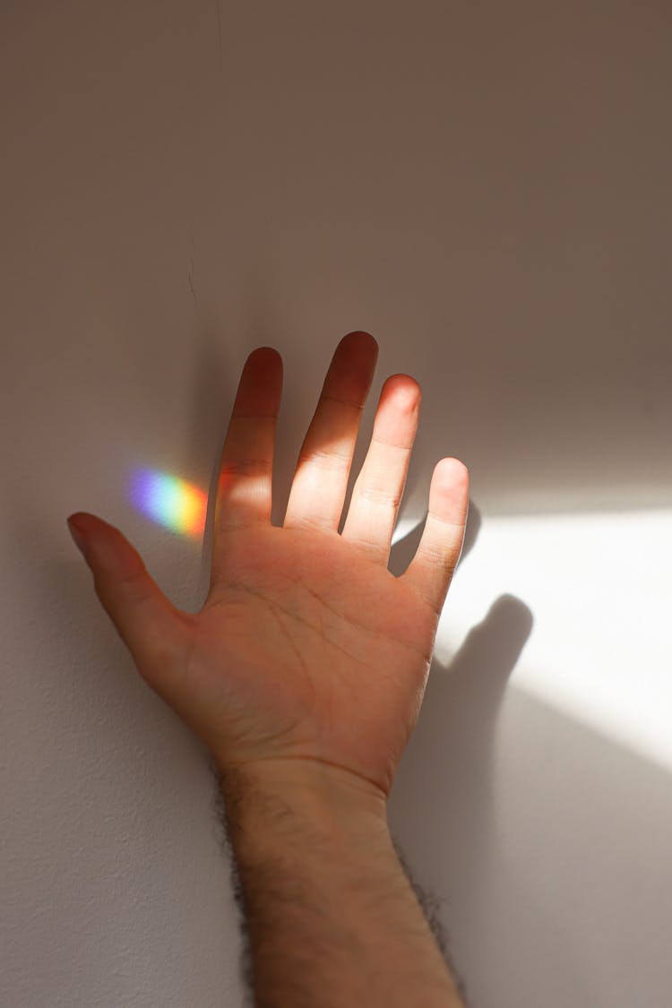 Rainbow Light On A White Wall Near A Hand