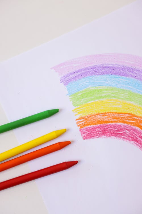 Colorful Crayons on a Bond Paper with Rainbow Drawing