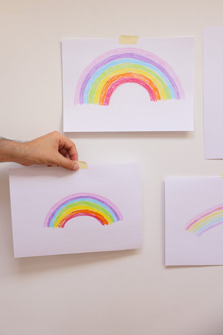 A Hand Posting An Artwork With Rainbow Drawing On Wall