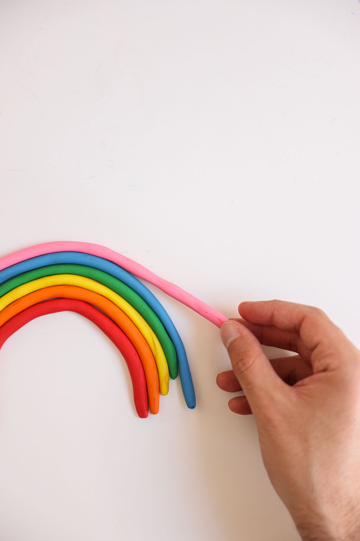 A hand arranging a colorful clay rainbow with clouds for a hanging mobile