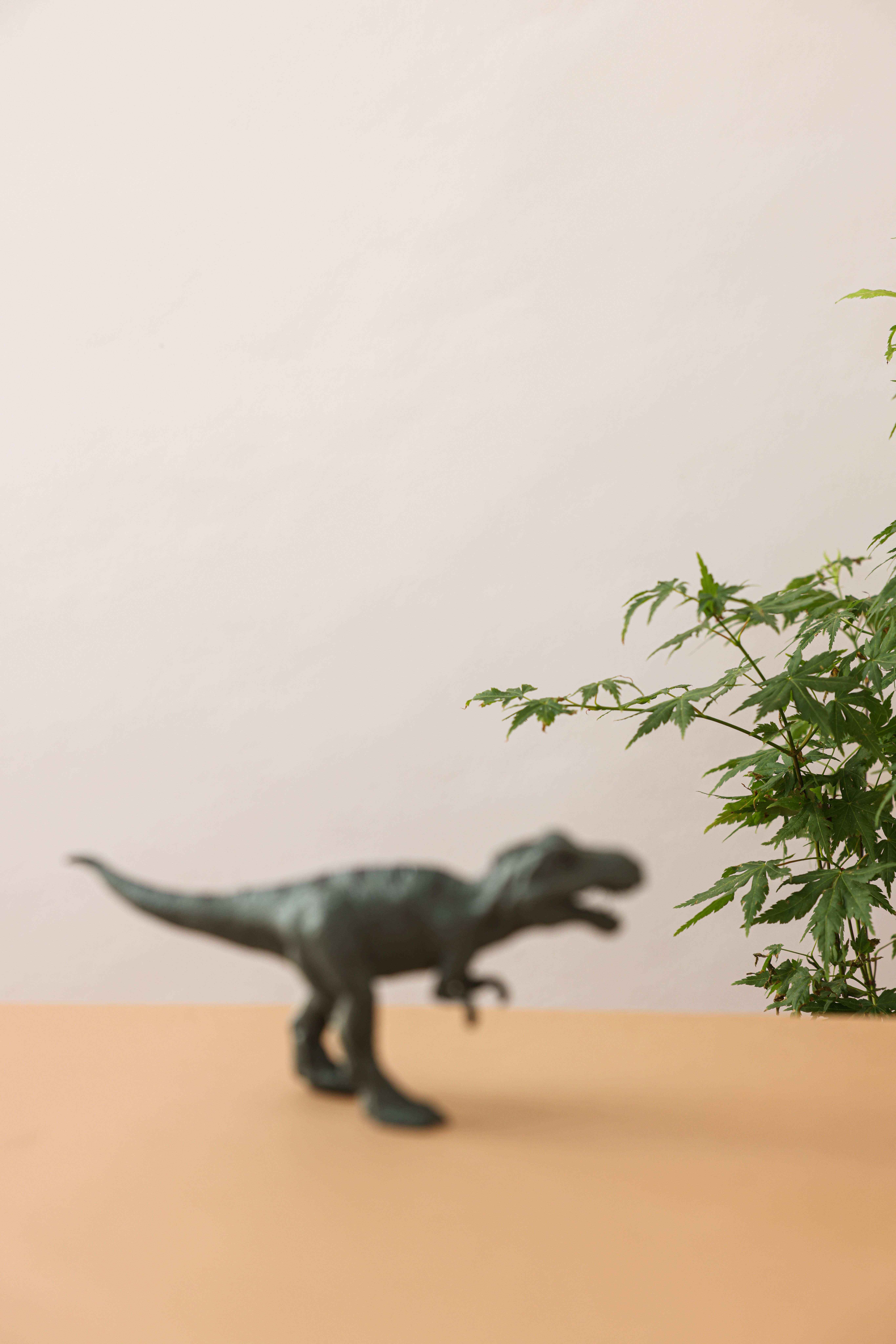 A blurred dinosaur toy on a table next to green foliage creating an artistic still life scene.