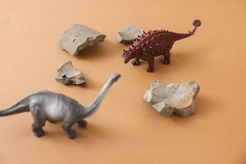 Free Close-up of plastic dinosaur toys and rocks on a beige background, ideal for creative projects. Stock Photo