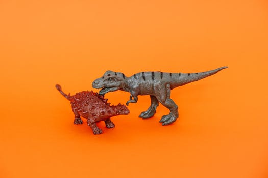 Two miniature dinosaur toys on a vibrant orange background.