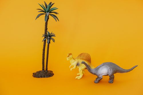 Free Colorful toy dinosaurs and palm trees on a vivid yellow backdrop, perfect for playful themes. Stock Photo