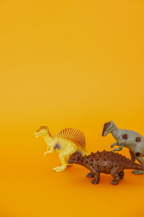 Free A trio of realistic dinosaur toys set against a bright orange background, highlighting playful creativity. Stock Photo