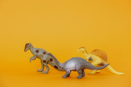 Free Three dinosaur toy figurines on a vibrant yellow background, ideal for playful concepts. Stock Photo