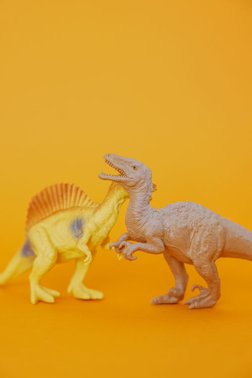 Free Two dinosaur toys on a vibrant yellow background, great for kids' themes. Stock Photo