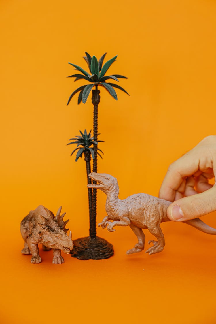 Hand Holding Plastic Dinosaur On Orange Background