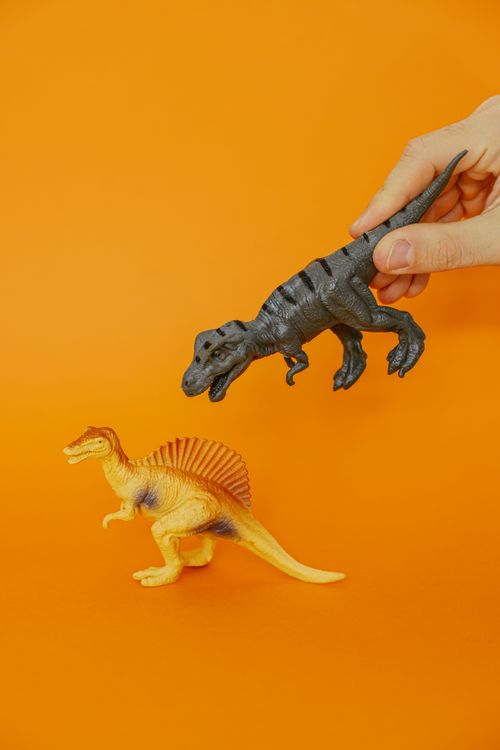Free Hand playing with toy dinosaurs on a vivid orange background, showcasing prehistoric fun. Stock Photo
