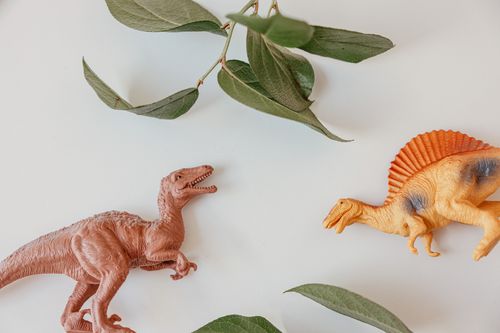 Free Two dinosaur figurines with leaves on a white background, minimalist style. Stock Photo
