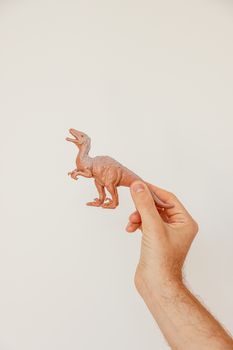 A hand holding a brown plastic dinosaur toy against a plain white background. Perfect for educational and creative uses.