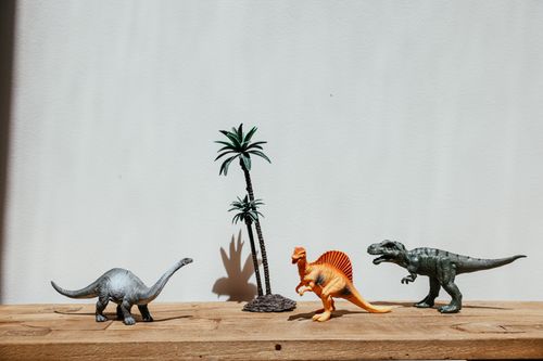 Free Colorful toy dinosaurs arranged with a palm tree on a wooden surface. Stock Photo
