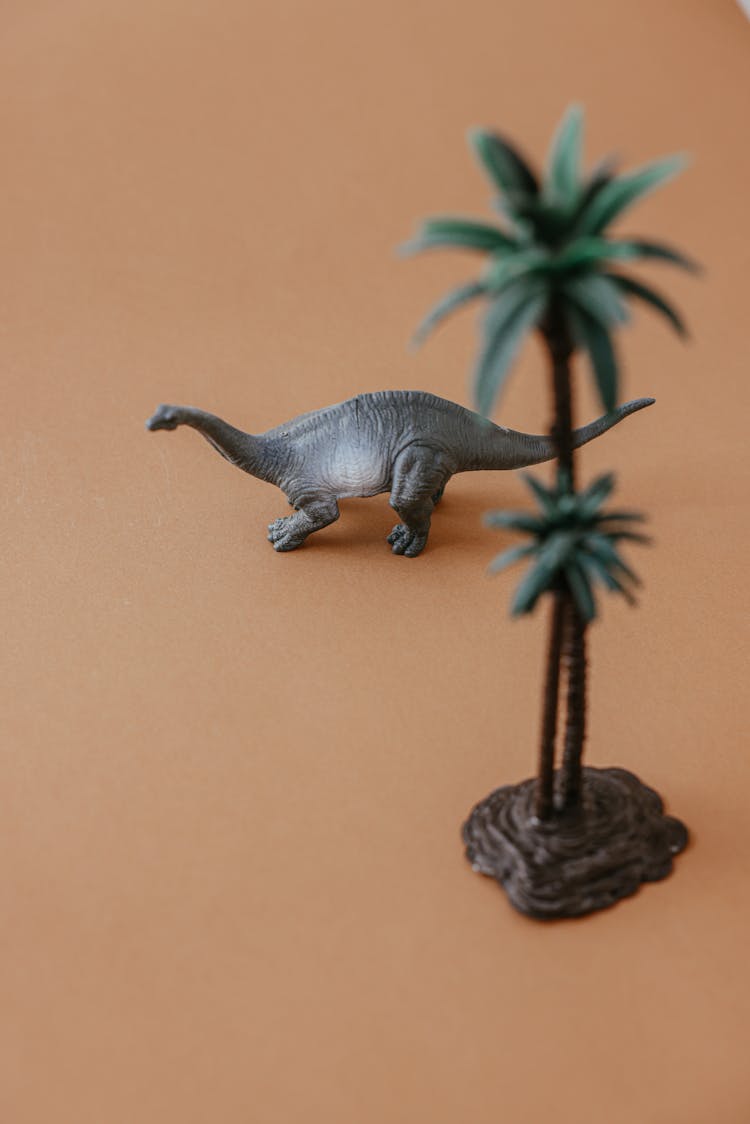 A Gray Toy Dinosaur Near A Palm Tree