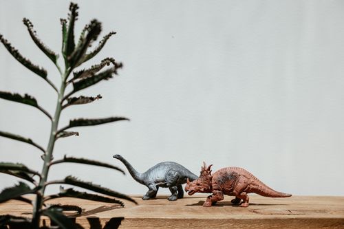 Free Colorful dinosaur toys with a plant on a wooden table, offering a playful prehistoric theme. Stock Photo
