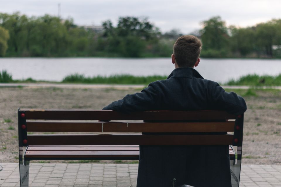 A man sitting alone on a bench looking out over a lake