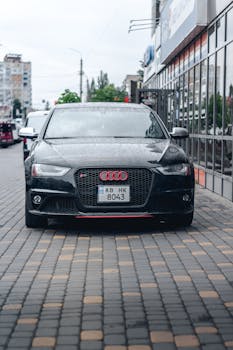 Front view of a sleek black car parked on an urban street during a cloudy day.