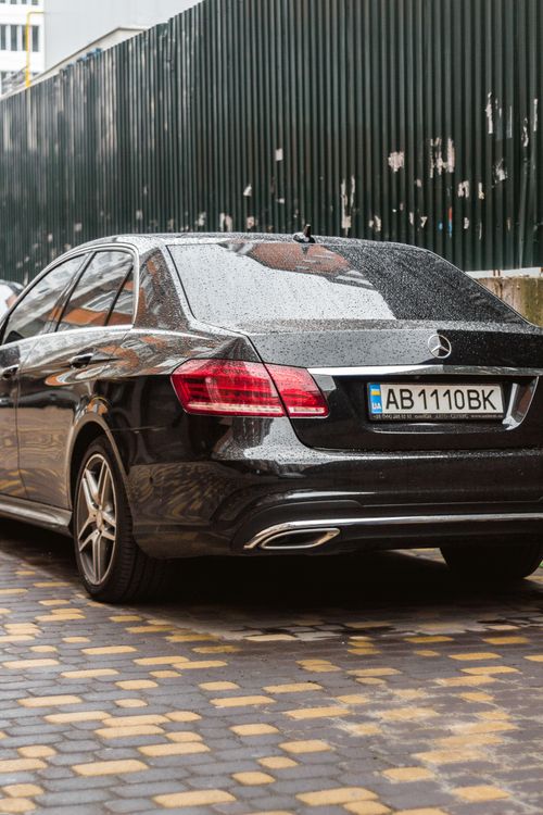 Free A sleek black car showcasing luxury and style, parked on a wet, cobbled street. Stock Photo