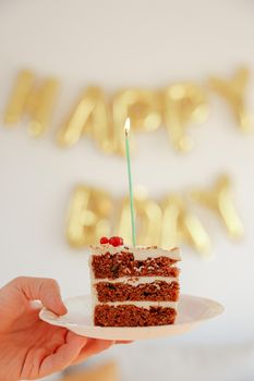 Close-up of a birthday cake slice with a candle against a festive backdrop.