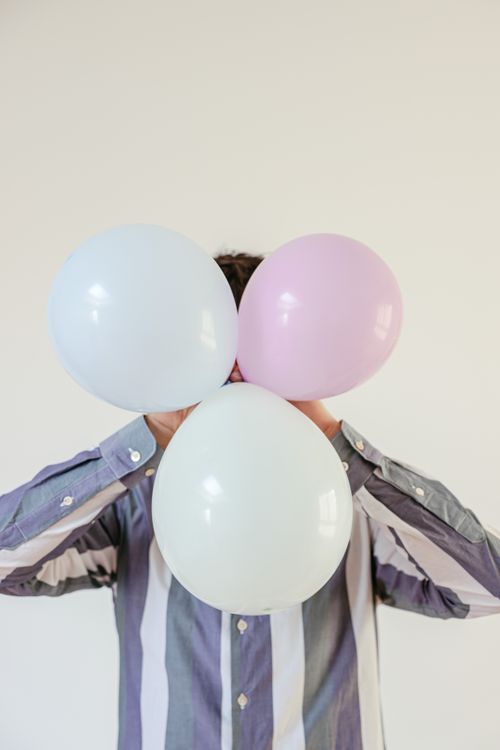 Free Adult hiding face with colorful balloons, white background. Stock Photo