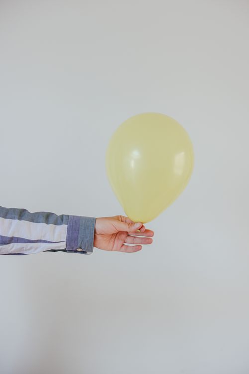 Free A close-up of a hand holding a yellow balloon with a white background, perfect for celebrations. Stock Photo